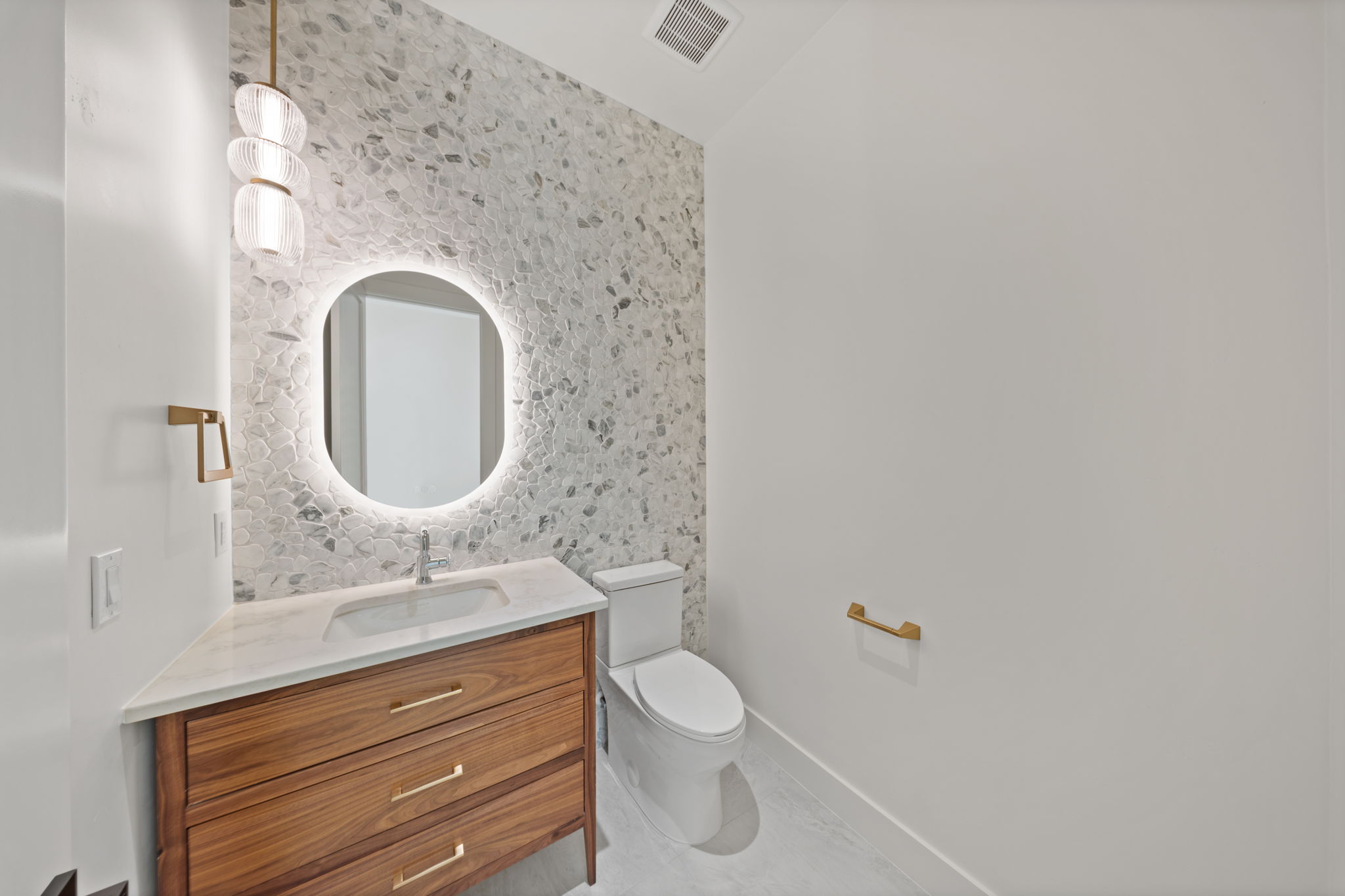 Finished bath at The Lookout with a wood vanity, stone tile, and an illuminated oval mirror