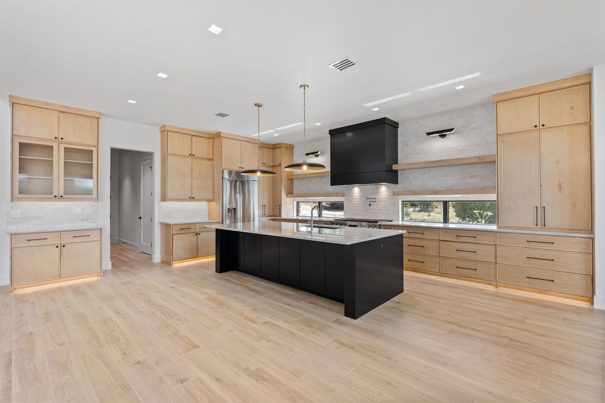 The Lookout's completed kitchen with light wood cabinetry, a black island, pendant lights, and a black range hood